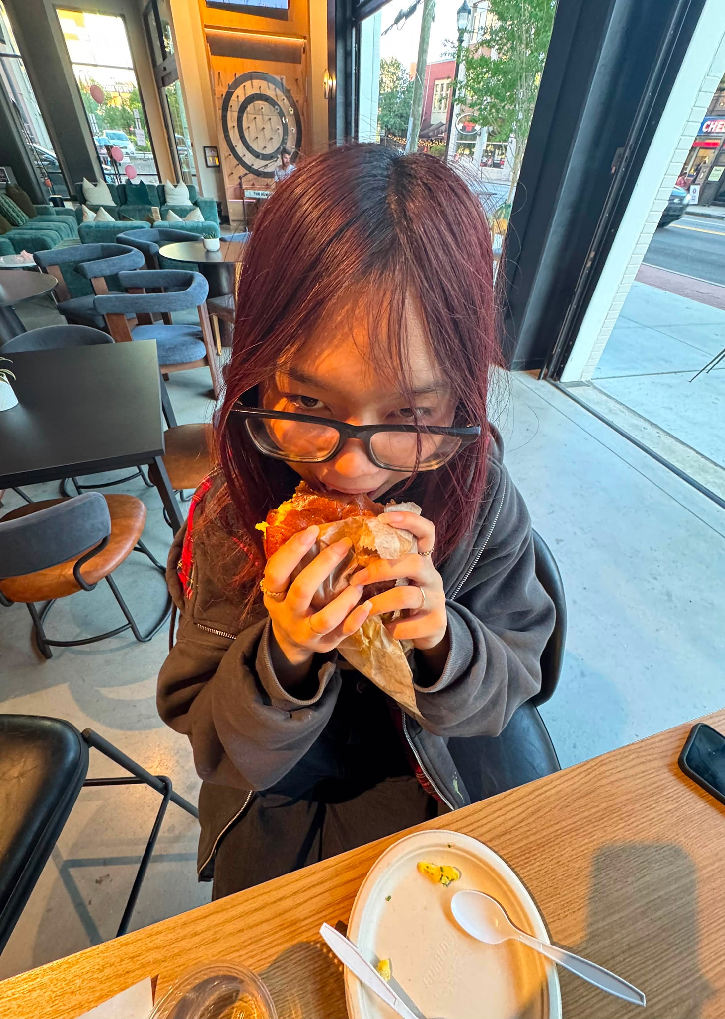 Tina Le eating a breakfast sandwich at an outdoor cafe table