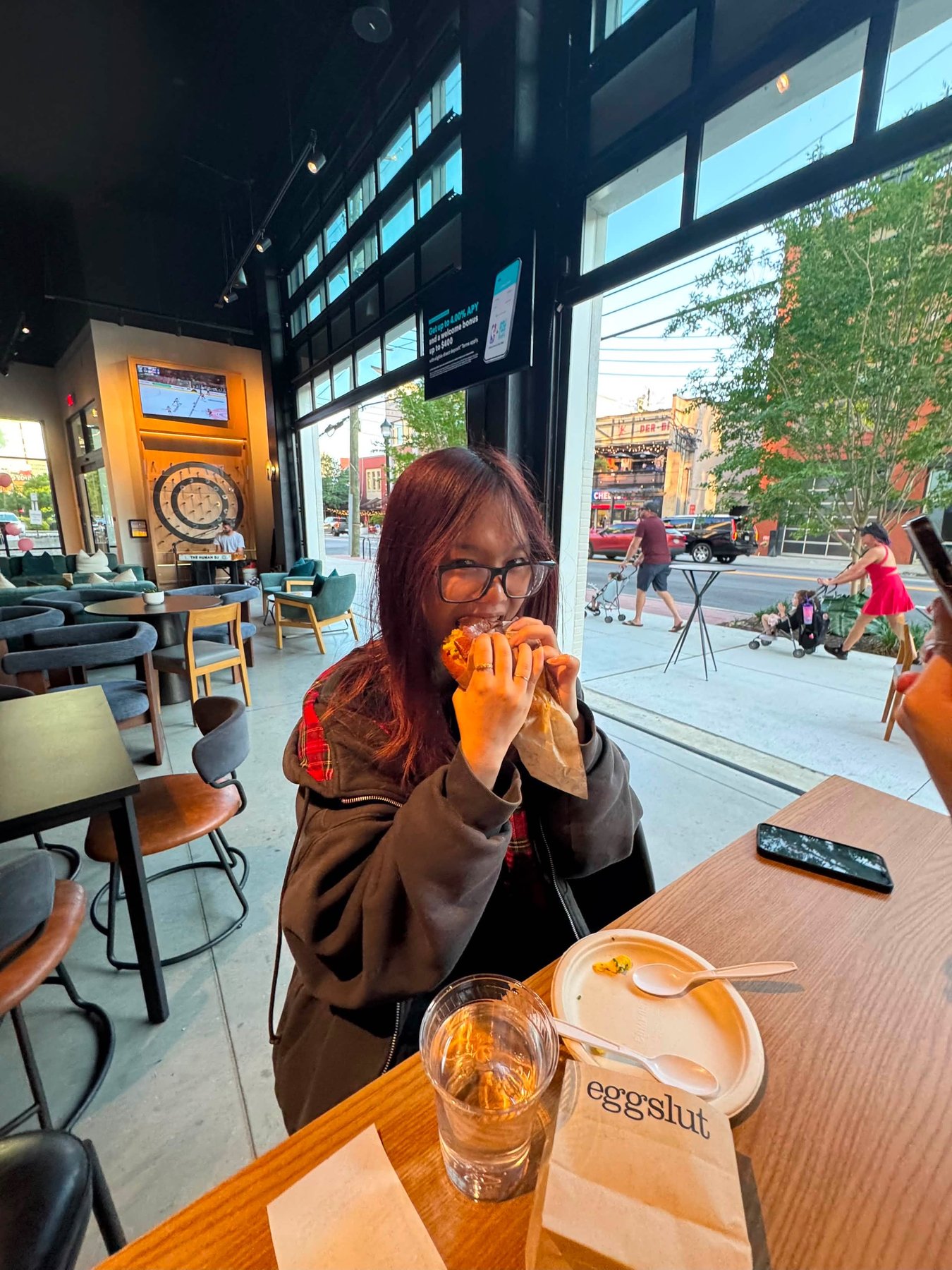 Tina Le taking a bite of a sandwich at a window counter inside eggslut
