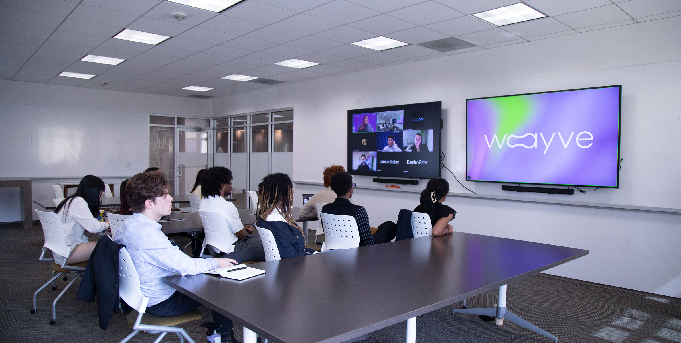 The Wayve team in a meeting room watching a video call, with the Wayve logo displayed on a second screen