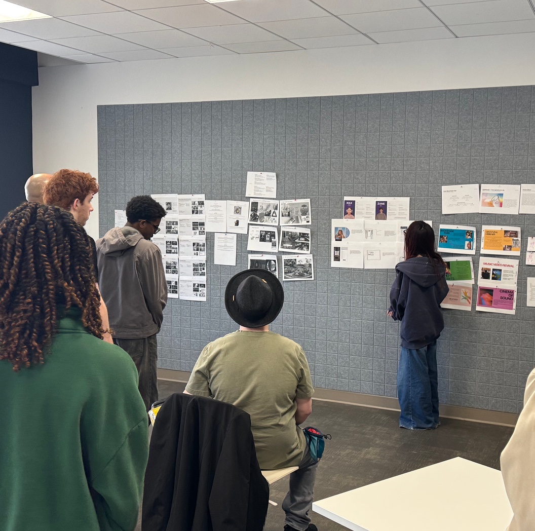 Students reviewing pinned-up research boards on a gallery wall